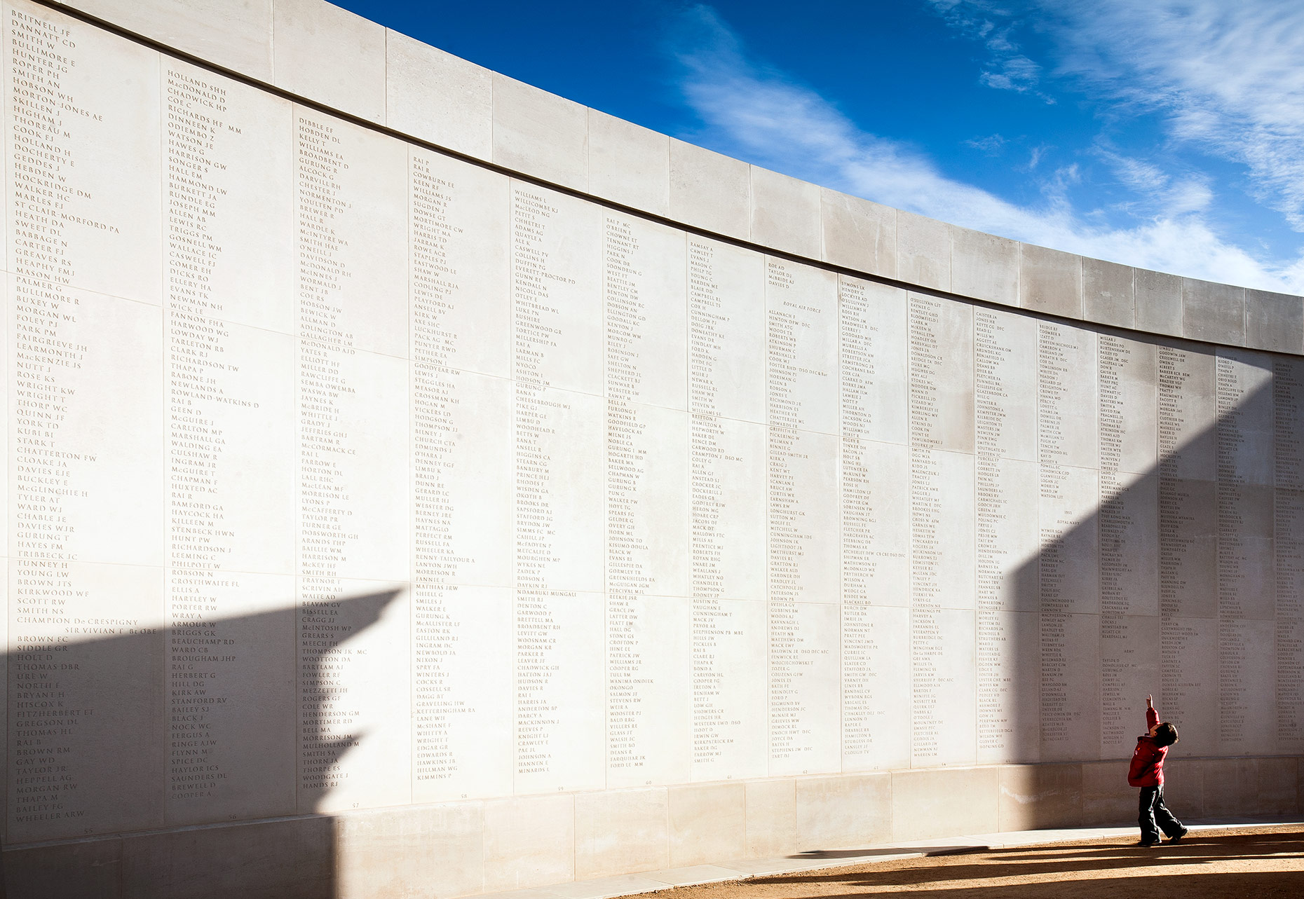 Editorial photography of a child in red coat pointing to names at The Armed Forces Memorial in Alrewas, Staffordshire.
